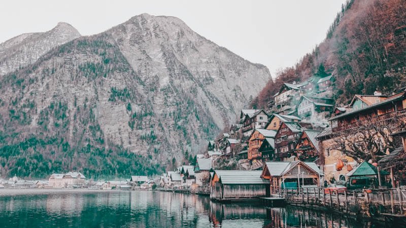 a mountainous winter village sat upon a lakeside during the fog.