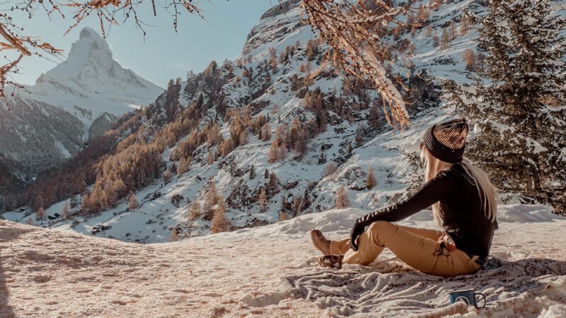 A woman bathed in golden hues, taking a break from skiing in Zermatt to enjoy the view of the Matterhorn.