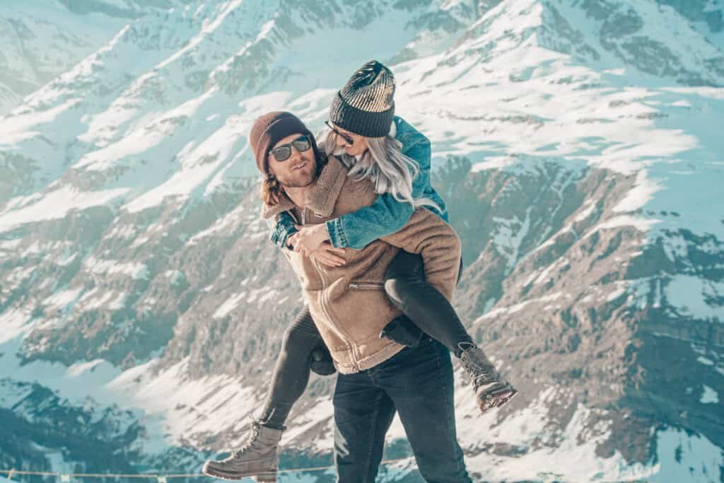 Woman getting a piggyback from a man in the snowy mountains.