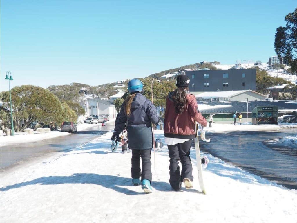 Two female snowboarders walking down the street in Mt Buller, Australia.