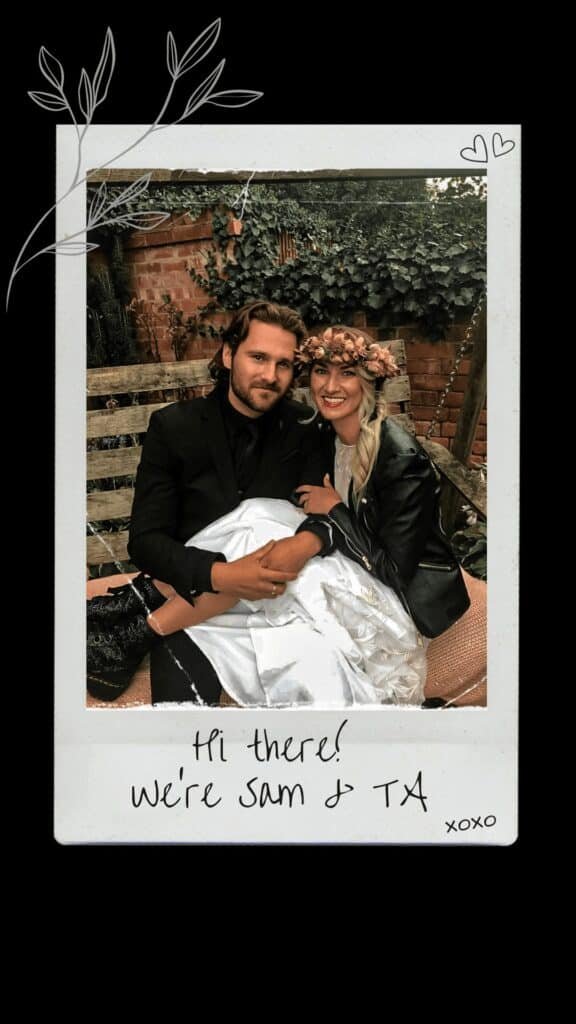 Sam in all black suit and TA in wedding dress, doc martens, leather jacket and flower crown, sat on a swing seat.