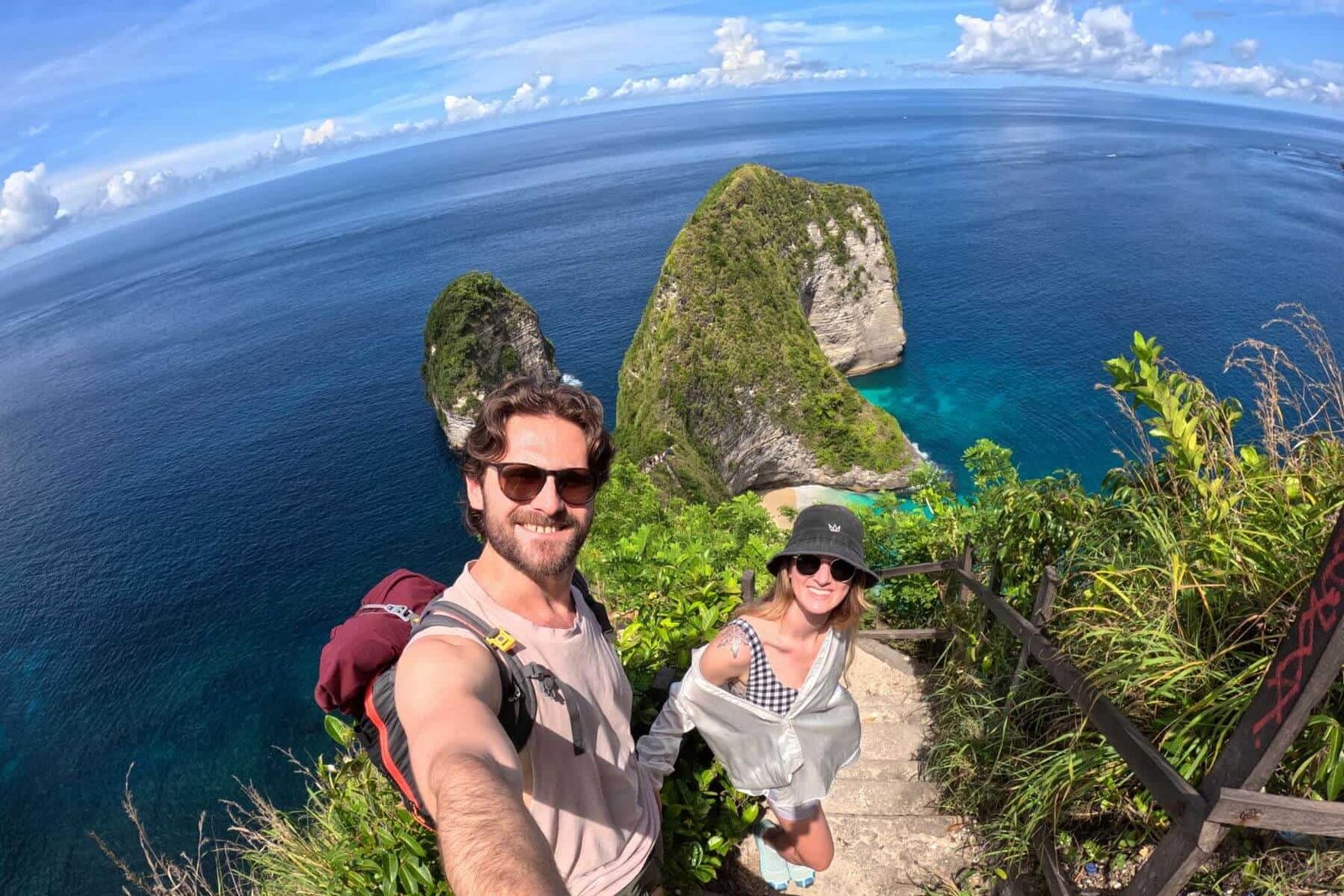 A woman and a man standing at the top of the staircase above Kelingking beach, the famous travel spot of the t-rex cliffs.