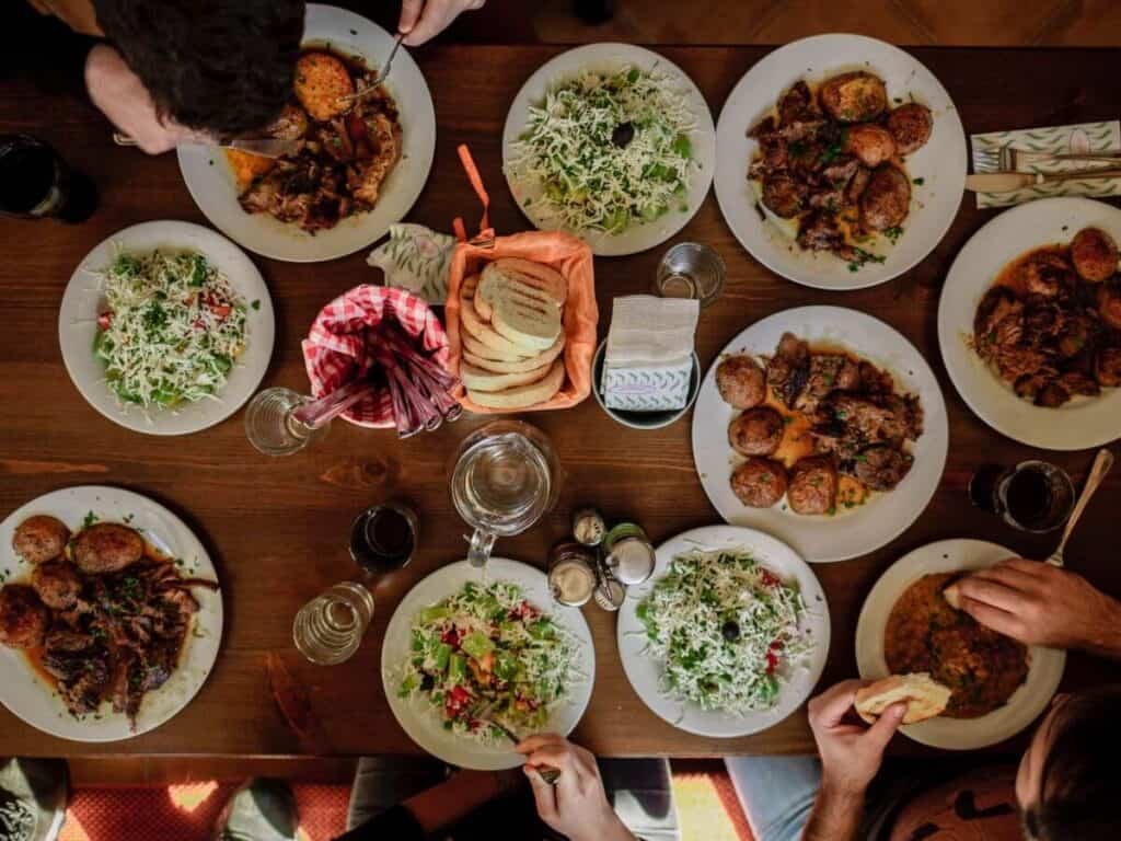 a table full of many plates of food consisting of traditional Bulgarian dishes of salad, bread and potatoes.