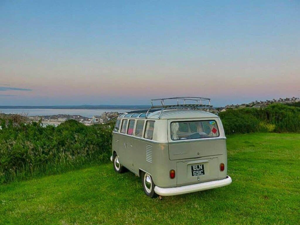 A classic VW campervan on a road trip in Cornwall, parked up overlooking St Ives beach.
