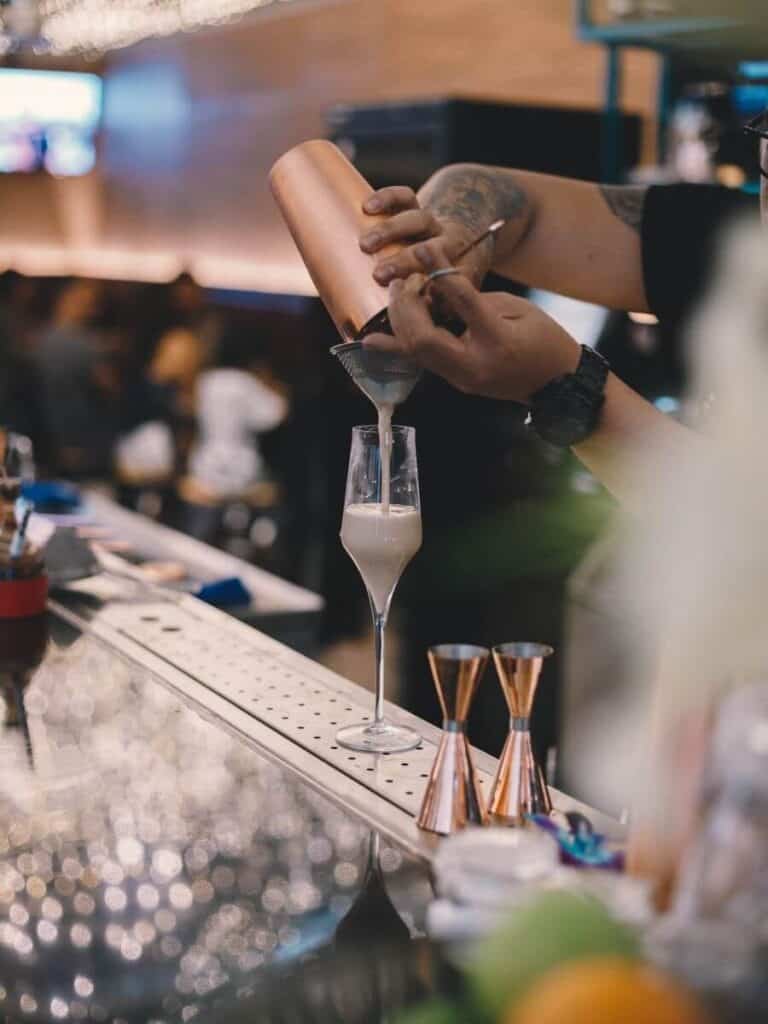 Bartender straining a milky white cocktail into a champagne flute during his seasonal work.