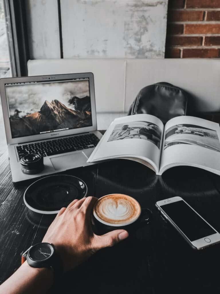 laptop, book, coffee and iphone laid out on a desk in a moody tone.