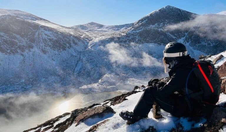 Woman in all black ski gear sat at the top of a loch in snowy Scotland.
