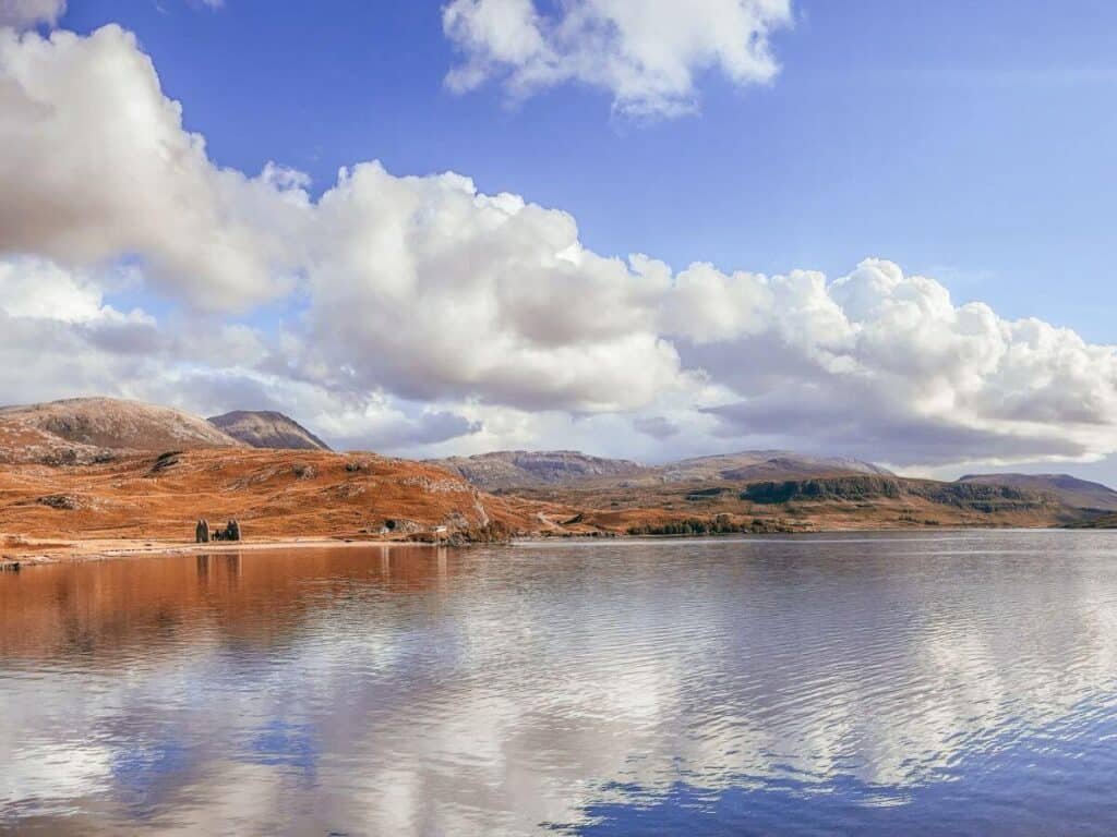 Loch Assynt and Ardvreck Castle on a beautiful blue sky day. Calm water and rusty tones.