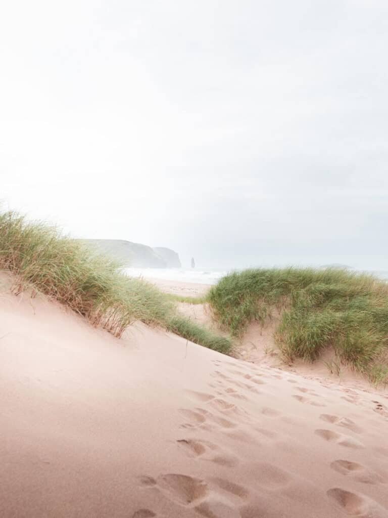 Sandwood bay in the distance of the grassy sandunes and footprints leading to the beach. The best beach for your NC500 Itinerary.