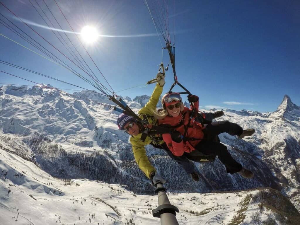 A tandem paraglider, flying over a snow covered Zermatt.