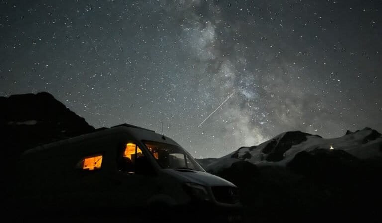 A campervan parked on the Süstenpass at night, underneath the milkyway and the Swiss Alps.