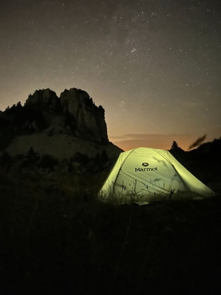 A tent lit up at night, underneath the stars and the mountain background of the Swiss Alps.