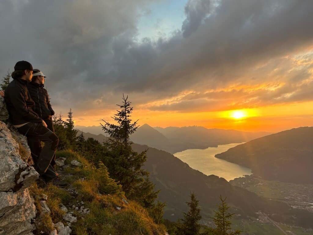 A couple standing on a mountainside overlooking Interlaken, Switzerland and the lake below at sunset.